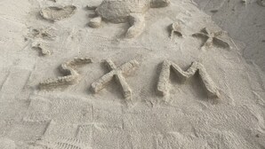 Una playa arenosa con huellas y la palabra "SXM" grabada en la arena.