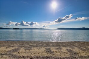 Ranta, jonka yllä on kirkas taivas ja jonka tyyni vesi heijastaa auringonvaloa.