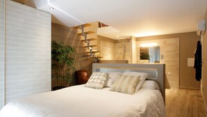 A modern bedroom with a large bed, a staircase, and a potted plant.