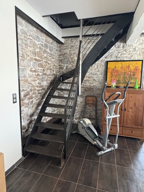 A staircase with a stone wall, a treadmill, and a wooden cabinet. - STUNNING STONE FARMHOUSE AMIDST THE VINEYARDS, 20 MINUTES FROM THE CITY OF CARCASSONNE (Ventenac-Cabardès)