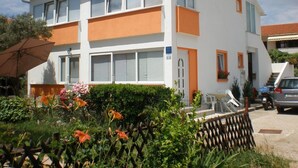 A two-story building with a white and orange facade, large windows, and a visible door. - Charming room Dijana with air conditioning & Wi-Fi (Krk)