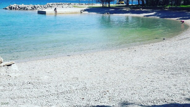 A pebble beach with clear water, a rocky breakwater, and a line of trees. - Charming room Dijana with air conditioning & Wi-Fi (Krk)