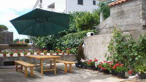 An outdoor patio with a wooden table and benches, surrounded by potted plants and a green umbrella. - Charming room Dijana with air conditioning & Wi-Fi (Krk)