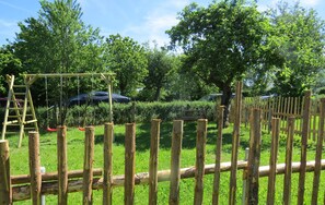 A wooden fence with a ladder and swings in a park.