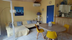 A room with a bed, a sofa, a dining table with yellow chairs, a lamp, and a painting on the wall. - house 4/5 pers near lake and ocean (HOURTIN)
