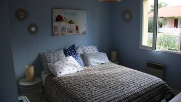 Une chambre à coucher avec une couvre-lit à motifs, un tableau représentant des parapluies et une fenêtre donnant sur un immeuble.