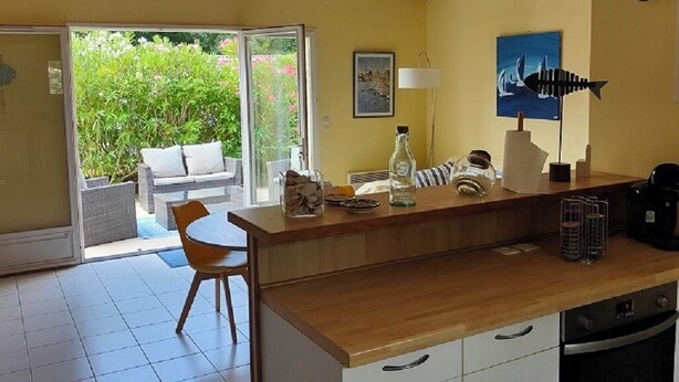 A kitchen with a wooden countertop, white cabinets, and a sliding glass door leading to a patio with outdoor furniture. - house 4/5 pers near lake and ocean (HOURTIN)