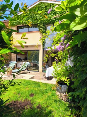 A patio with outdoor seating, a glass door entrance, and a garden with greenery and flowers. - Village house with swimming pool   (Lisle-Sur-Tarn)