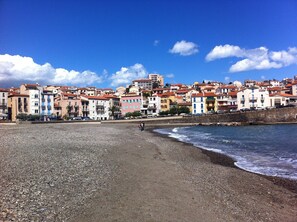 A coastal town with colorful buildings, a pebble beach, and a clear blue sky. - Large T2 duplex with character, all comfort, exceptional sea view (Banyuls-Sur-Mer)