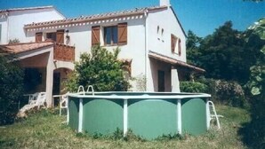 Une maison à deux étages avec un balcon, une piscine et un jardin.