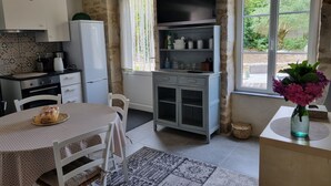 Una cocina con mesa de comedor, sillas, refrigerador, cafetera y ventana con vista a follaje.