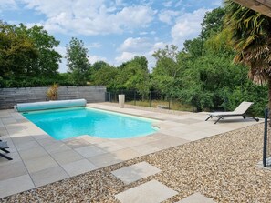 A rectangular swimming pool with a tiled deck, surrounded by a fence and trees.