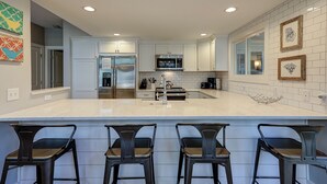 Una cocina moderna con una isla central, electrodomésticos de acero inoxidable y una zona de bar con taburetes.