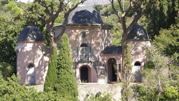 A historical building with a central dome and two smaller domes, surrounded by trees.