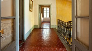 A hallway with a red-tiled floor, a wooden door on the left, and a black metal railing on the right.