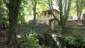 A stone bridge in a forested area with a small building in the background.