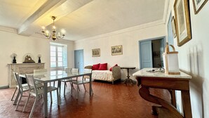 A dining area with a glass table and chairs, a sofa with red cushions, a chandelier, and a fireplace.