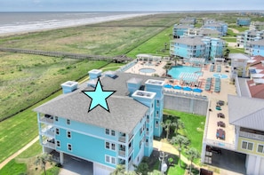 Un hotel frente al mar con varias edificaciones azules, un acceso peatonal a la playa y una zona de piscina.