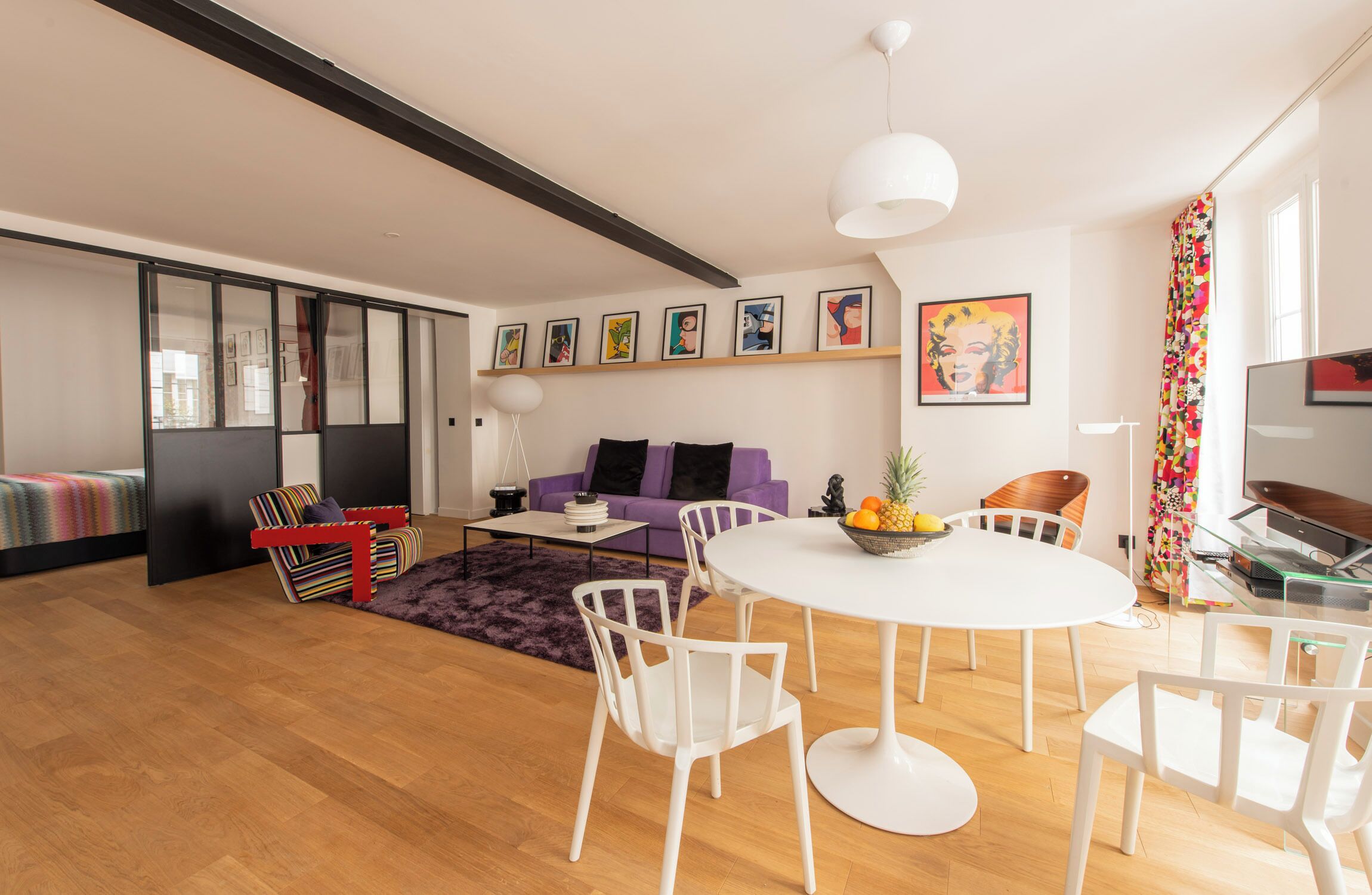 Una sala de estar moderna con una mesa redonda blanca, sillas blancas, un sofá púrpura y una mesa de centro de vidrio.