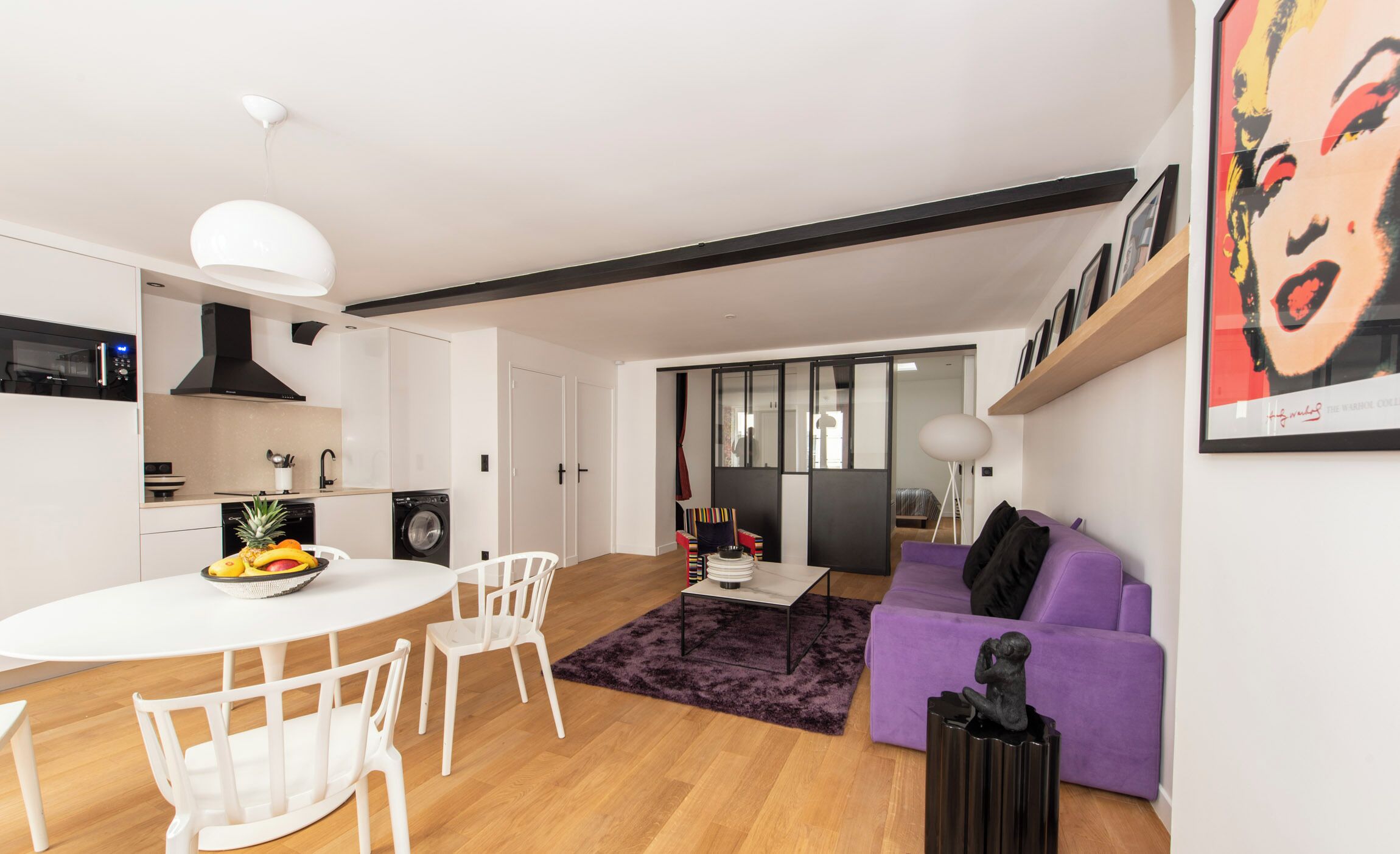 A modern living space with a kitchen, dining area, and a purple sofa.
