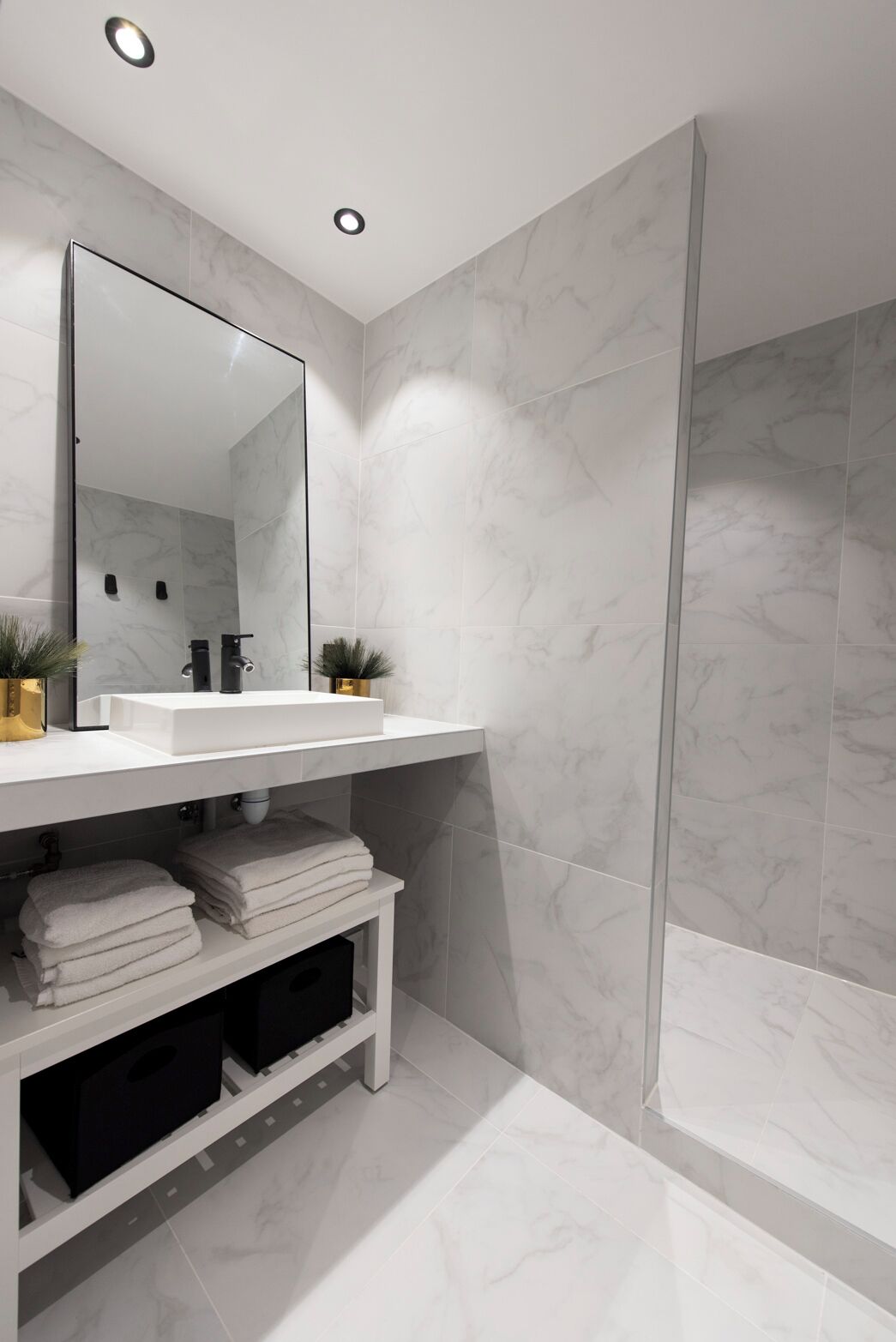 A modern bathroom with a white marble sink, a large mirror, and a glass shower enclosure.