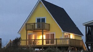 Une maison jaune avec un balcon, une terrasse et un petit porche.