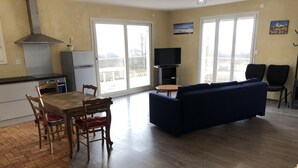 Un vaste espace de vie comprenant une table à manger en bois, un canapé bleu et un téléviseur à écran plat.