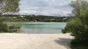 Une plage de galets qui mène à un lac paisible, avec des maisons en arrière-plan.