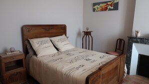 Ein ordentlich bezogenes Bett mit einem Holz-Kopfteil, zwei dekorativen Kissen, einem Nachttisch mit einer Lampe und einem kleinen Dekoartikel auf dem Beistelltisch.