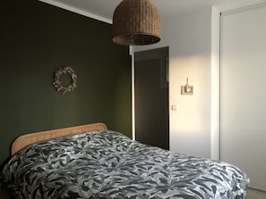 Un dormitorio con cama, lámpara de mimbre, un adorno de pared y una puerta.