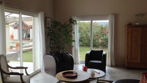 A spacious living room with a large sliding glass door leading to a patio, a black leather sofa, a wooden coffee table, and a wooden cabinet. - House with calm 140m ² with swimming pool 10x5 (Campagne)