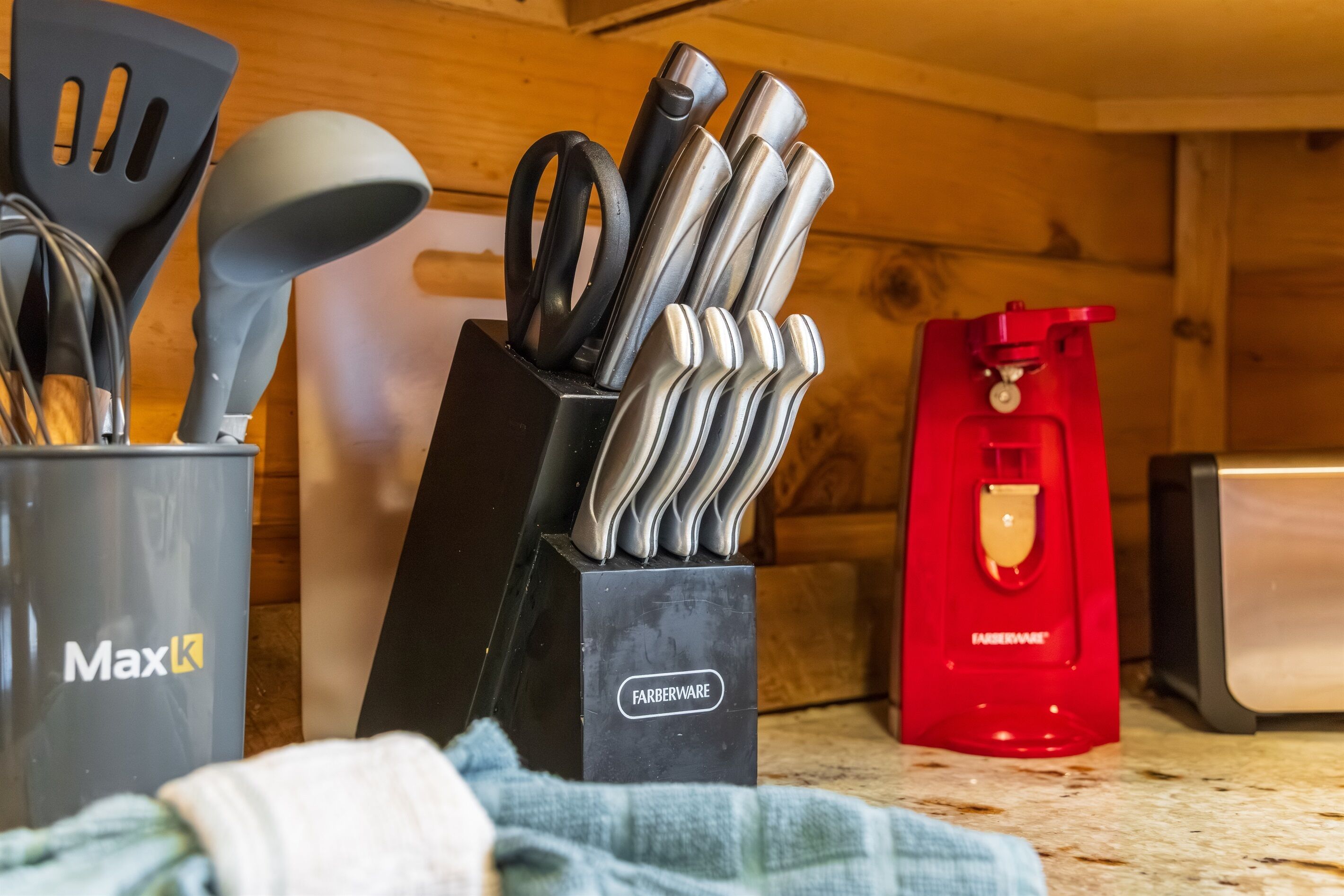 Una encimera de cocina con un bloque de cuchillos, un recipiente MaxK, un aparato Farberware y un dispositivo Farberware rojo.