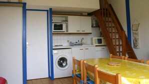 A compact kitchen with a washing machine, microwave, and wooden cabinets. - Cozy Vacation Home Near Beach with Garden, Parking, and WiFi (La Tranche-sur-Mer)