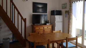 A dining area with a wooden table and chairs, a television, a refrigerator, and a clock on the wall. - Cozy Vacation Home Near Beach with Garden, Parking, and WiFi (La Tranche-sur-Mer)