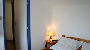 A bedroom with a bed, a bedside table with a lamp, and a door leading to another room. - Cozy Vacation Home Near Beach with Garden, Parking, and WiFi (La Tranche-sur-Mer)