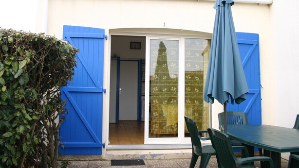 A small building with a tiled roof, a blue door, and a sliding glass door leading to an interior space. - Cozy Vacation Home Near Beach with Garden, Parking, and WiFi (La Tranche-sur-Mer)