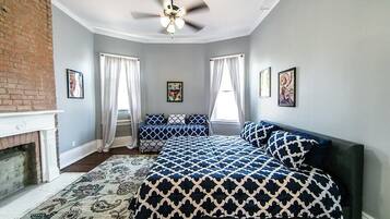 A bedroom with a bed, a fireplace, a ceiling fan, and artwork on the walls.