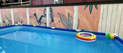 A swimming pool with a tiled floor, surrounded by a wooden fence with a mural.