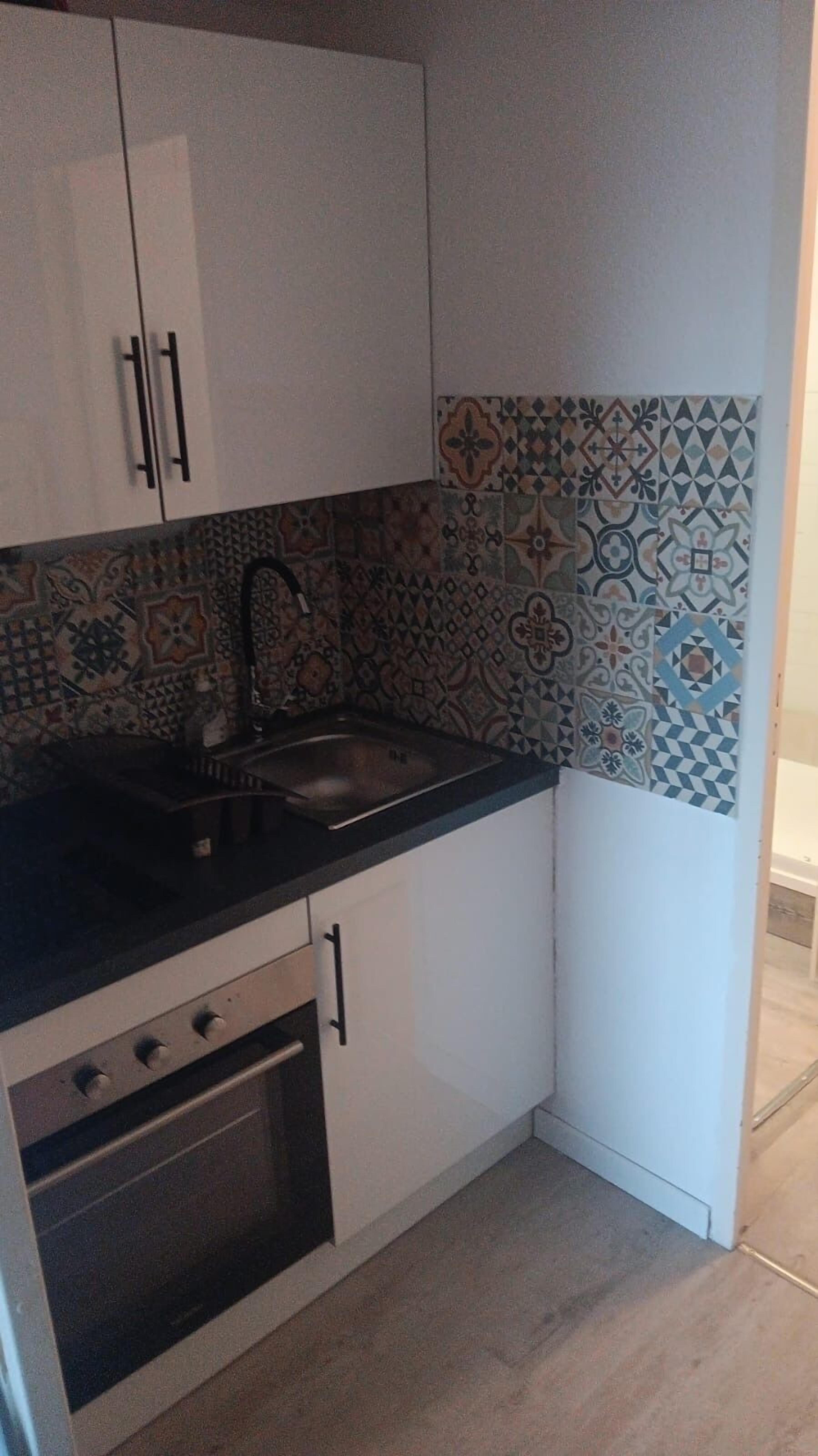 A compact kitchen with white cabinets, a black countertop, and a patterned backsplash.