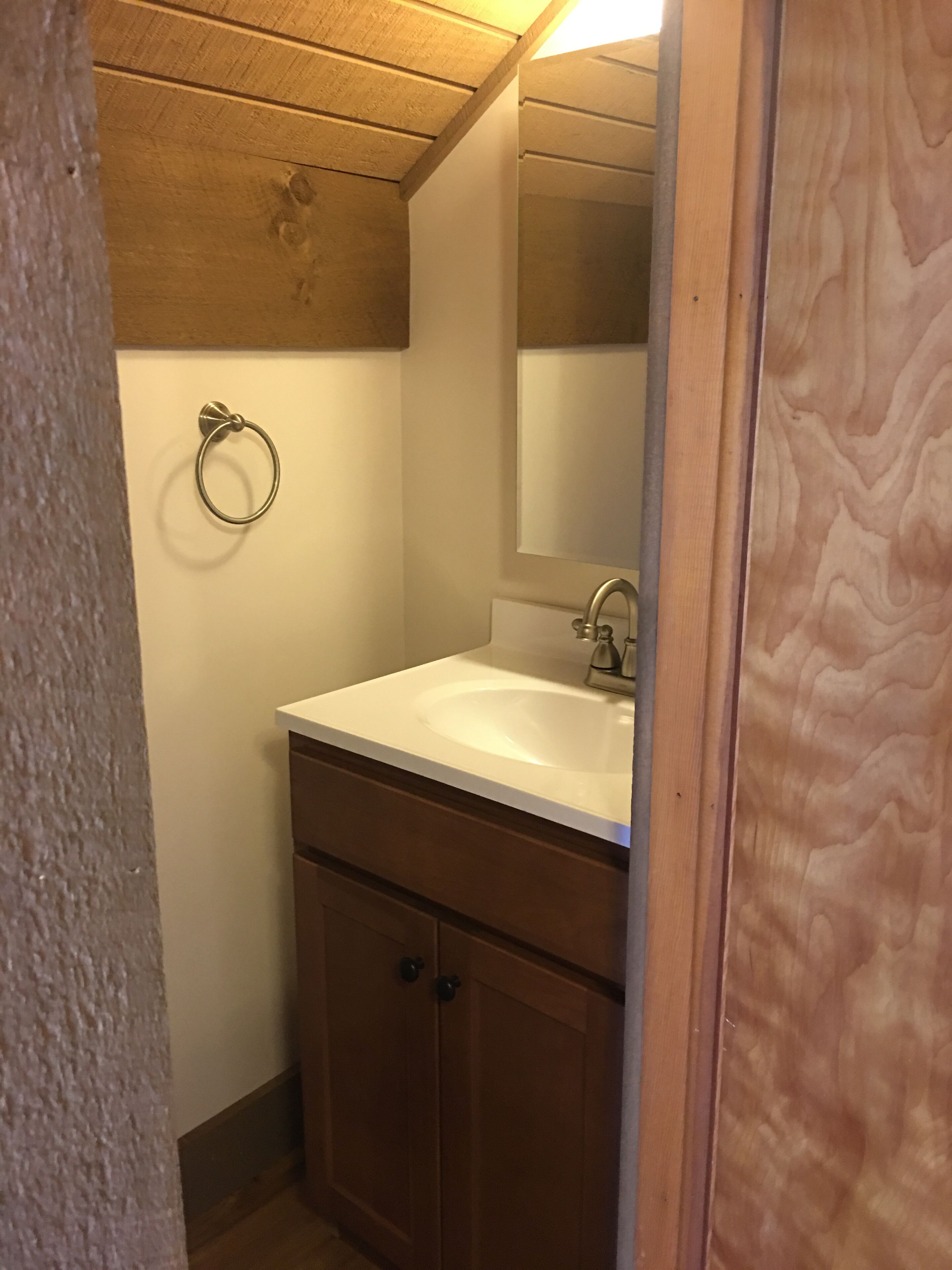 A small bathroom with a wooden ceiling, a white sink, a mirror, and a towel ring.