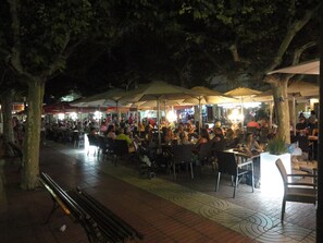 Un área de comedor al aire libre con varias mesas y sombrillas, rodeada de árboles.