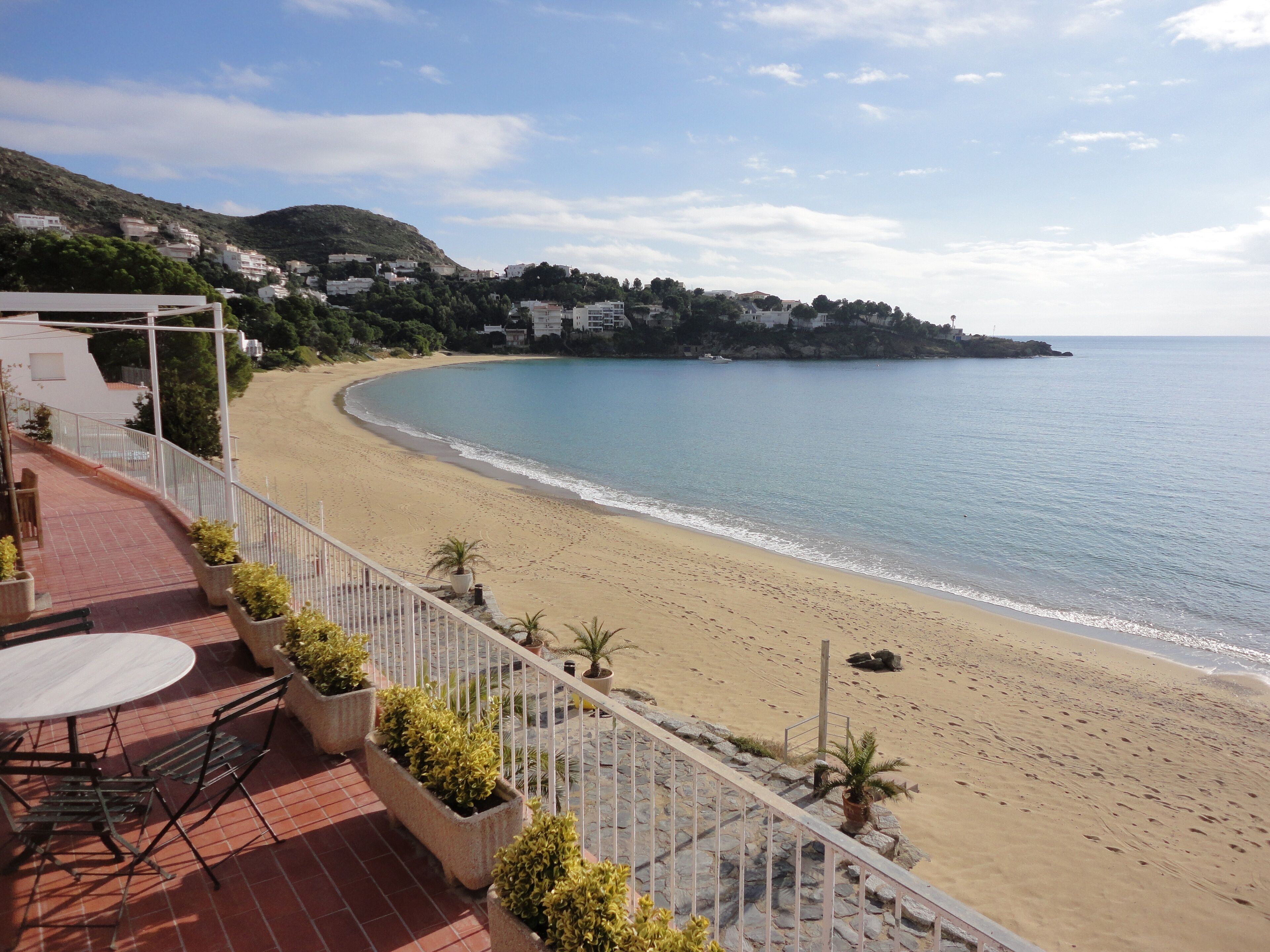 A beachside terrace with a table and chairs, overlooking a sandy beach and calm sea.