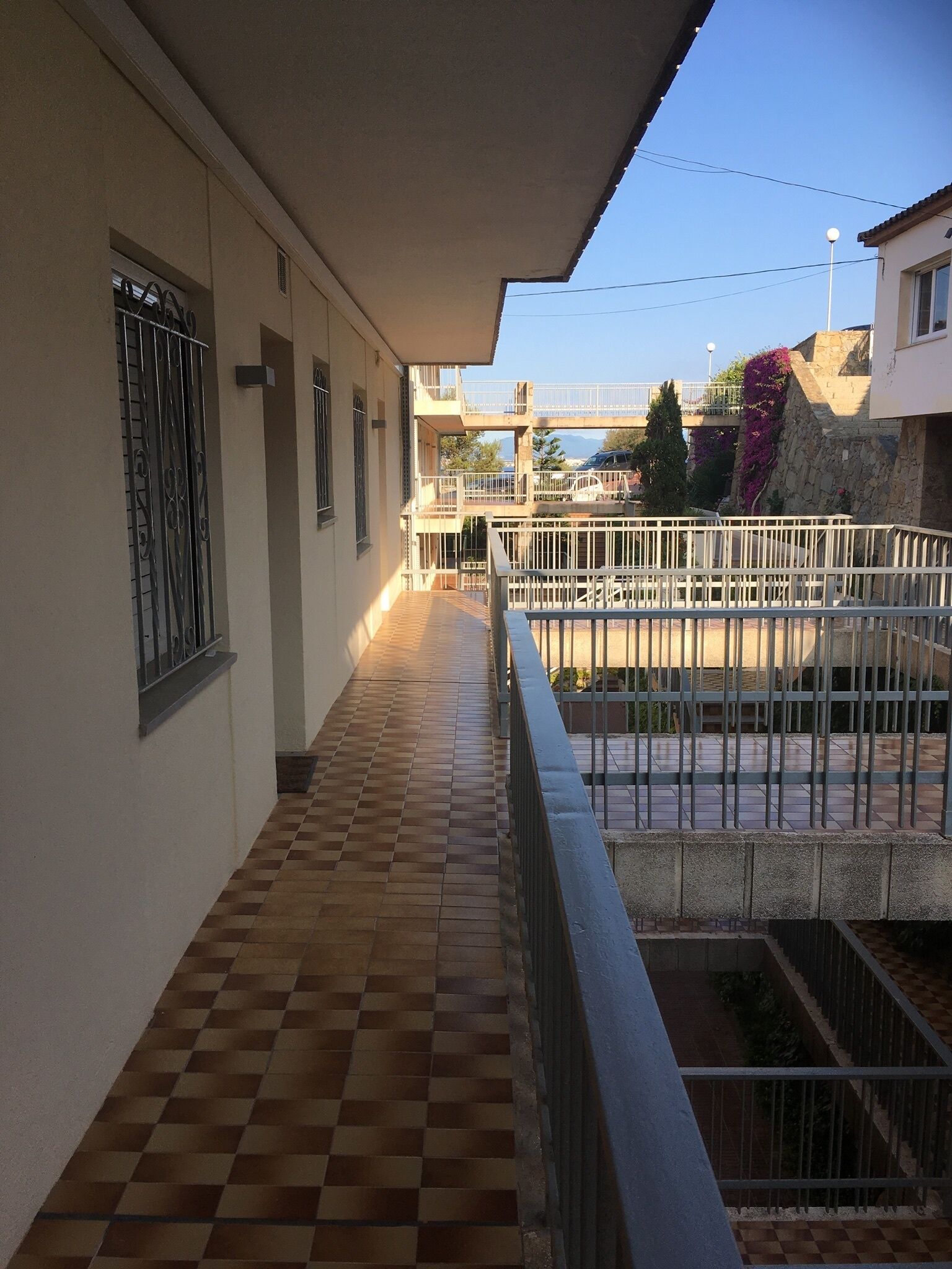 A corridor with a checkered floor leading to a balcony with a metal railing.