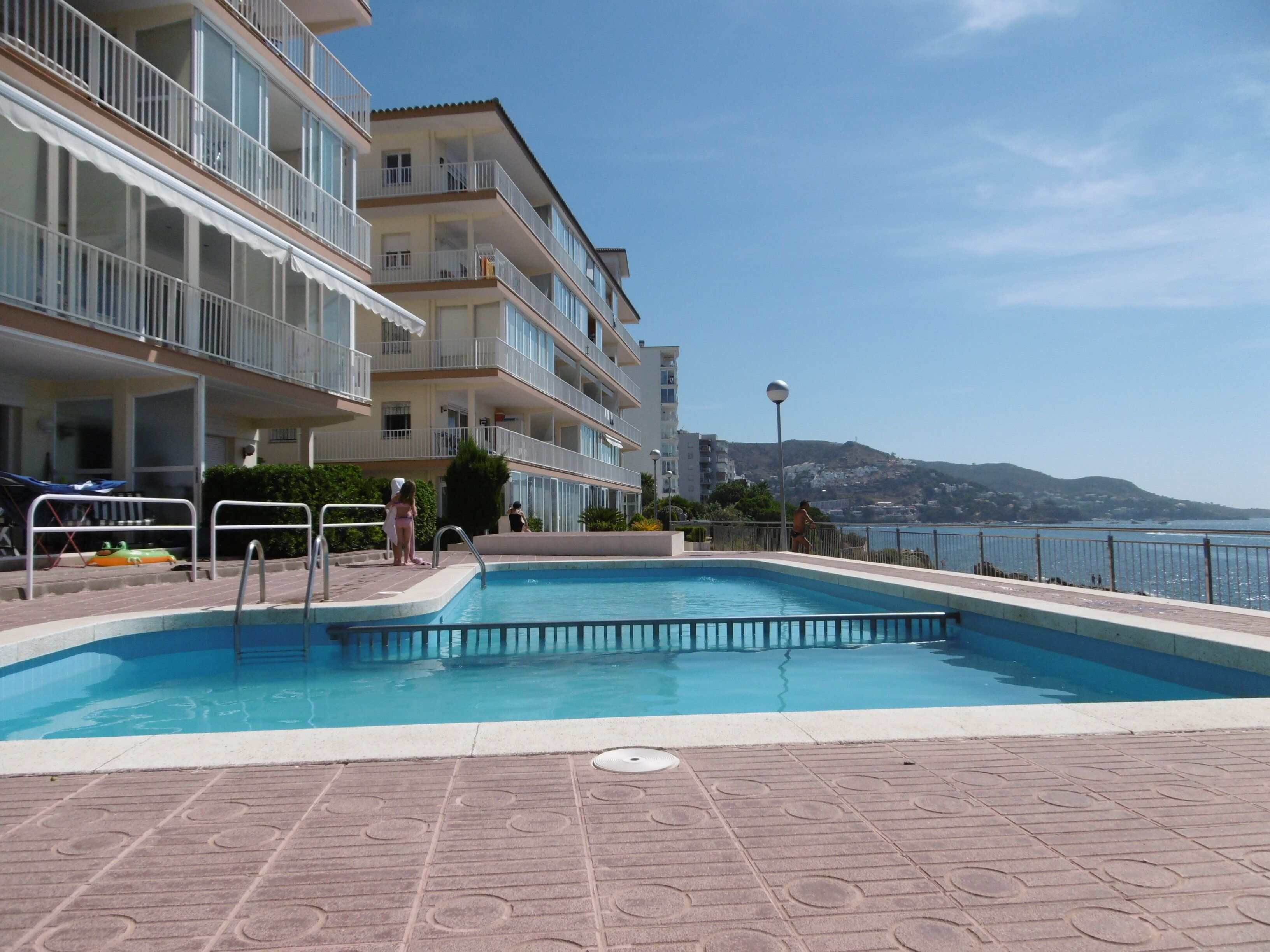 A swimming pool with a view of a coastal landscape, surrounded by a multi-story building with balconies.