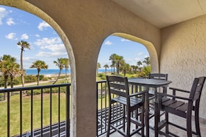 Un balcon avec une table et des chaises, donnant sur une plage et des palmiers.
