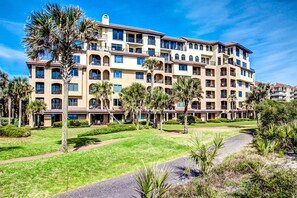 Un hôtel à plusieurs étages doté de balcons, de palmiers et d’une pelouse bien entretenue.