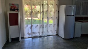 A kitchen with a refrigerator, a white cabinet, and a window with a leaf-patterned curtain.