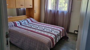 A bedroom with a bed, wooden wardrobe, and a window with curtains.