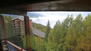 Vista desde un balcón sobre un área montañosa boscosa, con un edificio al fondo.