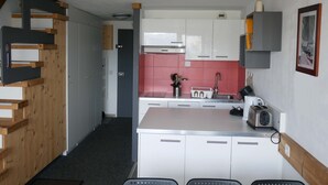Cocina compacta con gabinetes blancos, salpicadero rosa y techo de madera.